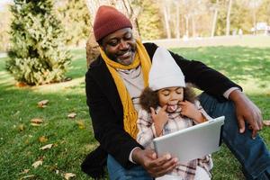 zwarte grootvader en kleindochter die tabletcomputer gebruiken terwijl ze in het park zitten