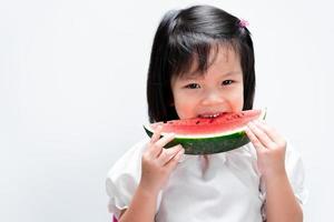 schattig aziatisch kindmeisje bijt om watermeloen te eten. op geïsoleerde witte achtergrond.