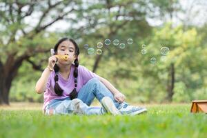 meisje zittend in de park met blazen lucht bubbel, omringd door groen en natuur foto