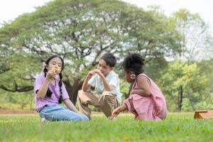 kinderen zittend in de park met blazen lucht bubbel, omringd door groen en natuur foto