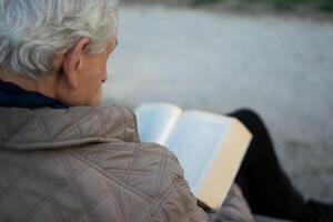 oud Mens met grijs haar- lezing een boek gelokaliseerd Aan een bank. foto