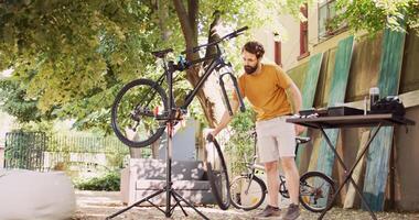 atletisch toegewijd Mens vaststelling beschadigd fiets met gespecialiseerd uitrusting van gereedschapskist in tuin. gezond Kaukasisch mannetje ontmanteling wiel en onderhoud fiets voorkant vork. terugtrekken schot. foto