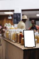 detailopname van telefoon tablet weergeven een geïsoleerd copyspace sjabloon is gezien Bij een eco vriendelijk voedsel winkel. gefocust beeld van een digitaal apparaat met een leeg mockup Scherm, geplaatst in de buurt bio-voedsel producten. foto