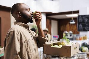 jong Mens inhaleert geur van een appel, bewonderend biologisch fruit en groenten. kruidenier op te slaan ondersteunt lokaal producenten, aanbieden bulk opties en bevorderen duurzaamheid en nul afval. kant visie schot. foto