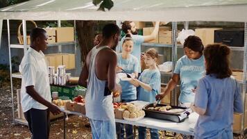 Kaukasisch meisje vrijwilligerswerk door overhandigen uit vrij voedsel naar behoeftig Bij non-profit voedsel rit evenement. groep van vrijwilligers het verstrekken van humanitair steun naar dakloos mensen en die in armoede. antenne, handbediend. foto