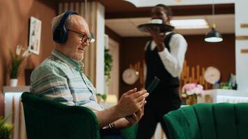 senior volwassen aan het kijken film Aan tablet en genieten van internet streaming Diensten in hotel lobby. toerist gebruik makend van apparaat naar houden omhoog met favoriete TV serie, aan het wachten voor controleren in werkwijze Aan bank. foto