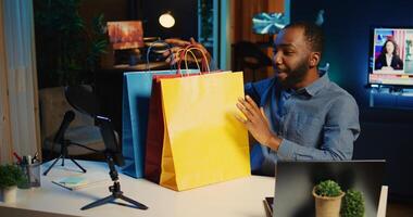 inhoud Schepper Holding boodschappen doen Tassen, filmen halen video in vaag lit studio. internet ster uitpakken kleding items hij gekocht, herzien mode winkels handelswaar, gebruik makend van professioneel camera foto