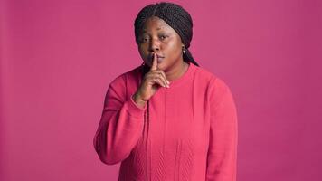 Afrikaanse Amerikaans vrouw staand in voorkant van geïsoleerd achtergrond uitdrukken met hand- gebaren. vrouw mode blogger op zoek Bij camera en gezegde stil zwijgen met vinger Aan haar mond. foto