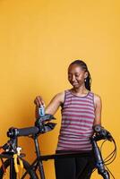 jeugdig vrouw fietser van Afrikaanse Amerikaans etniciteit inspecteert gebroken fiets componenten met hulpmiddelen. zwart vrouw vakkundig en precies regelen van reparatie staan voor fiets aanpassingen en onderhoud. foto