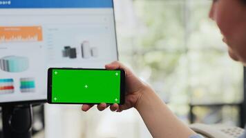 specialist looks Bij groene scherm Scherm Aan mobiel telefoon, Holding apparaatje met copyspace geïsoleerd software Bij werkstation. werknemer werken met blanco mockup lay-out in bedrijf kantoor. dichtbij omhoog. foto