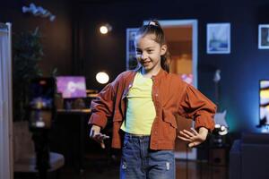 jong gen z inhoud Schepper in vaag lit huis studio dansen voor online volgers. klein meisje doet virale dans choreografie in neon lit leven kamer, filmen met mobiele telefoon foto