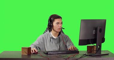 jong gamer zittend Bij computer bureau en spelen web gebaseerd video spellen met mensen, gebruik makend van modern gadgets naar hebben een mooi zo tijd. Aziatisch persoon concurrerende in rpg wedstrijd over- groene scherm. foto