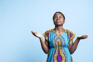 Afrikaanse Amerikaans vrouw interactie met Jezus door gezegde elegantie, geestelijk persoon met geloof bidden naar god tegen blauw achtergrond in studio. religieus vrouw model- gezegde een gebed. foto