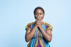 Afrikaanse Amerikaans model- aan het bedekken haar mond naar worden stil, herscheppen drie wijs apen symbool naar houden stil in voorkant van de camera. vrouw tonen inspirerend traditioneel teken in studio. foto