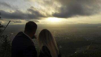 paar looks Bij stad- Bij ochtendgloren. klem. Mens shows vrouw stad met zon Aan horizon. mooi landschap met paar Aan berg met uitzicht stad- Bij dageraad foto