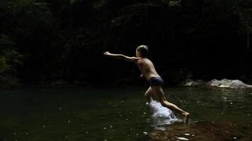 langzaam beweging van een jongen jumping in een waterval en natuurlijk vijver. creatief. jong jongen kind hebben pret in oerwouden. foto