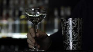 dichtbij omhoog van een barman zetten ijs kubussen in de klein leeg cocktail glas. media. details van maken een drinken met wazig flessen van alcohol Aan de achtergrond. foto