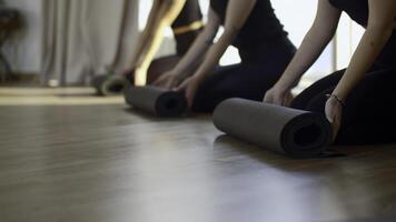 dichtbij omhoog van vrouw sport- groep rollend matten naar begin pilates. media. begin van opdrachten en geschiktheid Aan vloer. foto