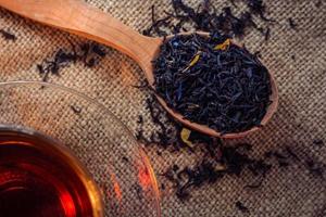 Droge bladeren van thee met additieven en gezette thee in een glazen beker op een donkere achtergrond van jute foto