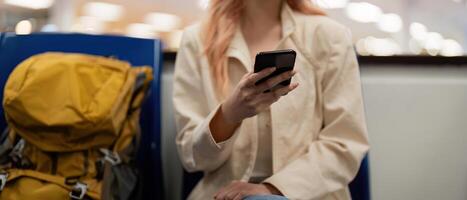 toerist vrouw gebruik makend van mobiel smartphone met koffer op reis tussen wacht voor vlucht in luchthaven terminal, vlucht controleren in, toerist reis reis concept foto