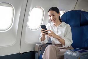 op reis en technologie. vliegend Bij eerste klas. jong bedrijf vrouw passagier gebruik makend van smartphone terwijl zittend in vliegtuig vlucht foto