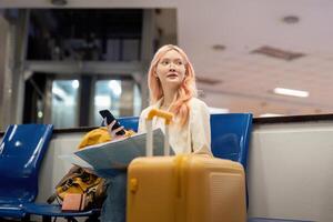 gelukkig jong vrouw Aziatisch is zittend in luchthaven in de buurt koffer en lezing kaart foto