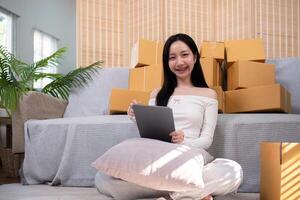 Aziatisch vrouw klein bedrijf ondernemer werken van huis gebruik tablet voor reclame inspectie. online afzet verpakking doos, concept ecommerce foto