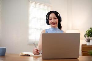 gelukkig jong vrouw Aziatisch in hoofdtelefoons en laptop maken notities, meisje leerling pratend door video conferentie telefoongesprek, online opleiding foto