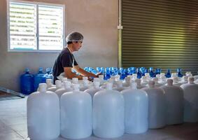 jong Mens arbeider of kwaliteit inspecteur in werkkleding werken in controle drinken water gallon in drinken water fabriek voordat zending.drinken water zakelijk, klein bedrijf, winkel, magazijn foto