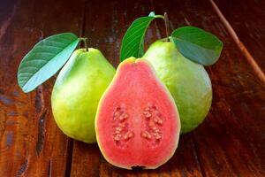 detailopname guava fruit, roze, vers, biologisch, met bladeren, geheel en gesneden, Aan rustiek houten tafel foto