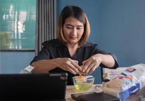 Aziatisch vrouw kraken een ei in meel naar maken bakkerij en koekjes studie online door tablet, genieten hobby Aan vakantie, idee van eigengemaakt voedsel. foto