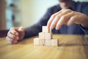 hand- strategisch plaatsen houten blokken in een traptrede ontwerp Aan een tafel, betekenend progressief succes en groei foto