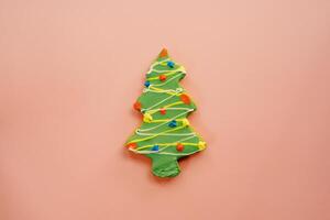groen geglazuurd Kerstmis boom koekje met kleurrijk slingers Aan een roze achtergrond foto