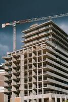 toren kraan bovenstaand een appartement gebouw onder bouw tegen een stormachtig lucht foto