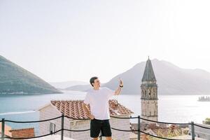 glimlachen vent duurt een selfie terwijl staand Aan een platform met uitzicht de baai van kotor. perast, Montenegro foto