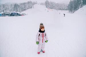 weinig glimlachen kind staand Aan een besneeuwd ski helling foto