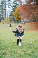 weinig meisje met vliegend haar- loopt langs de rand van de herfst Woud na haar moeder. terug visie foto