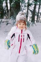 weinig meisje in een ski pak en een besneeuwd hoed wandelingen door de winter Woud foto