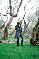 mam met een weinig meisje in haar armen wandelingen door een groen park tussen de bomen foto