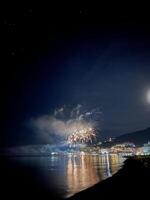 feestelijk vuurwerk in de donker lucht over- de verlichte stad- door de zee foto