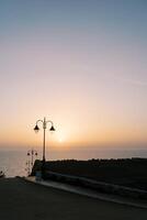 lantaarns langs de weg aflopend naar de zee Bij zonsondergang foto