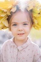 weinig verrast meisje vervelend een kroon van geel bladeren. portret foto