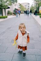 weinig meisje draagt een banaan huid naar beneden de straat foto