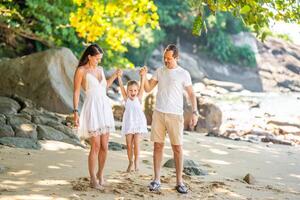 gelukkig jong familie van drie nemen een wandelen Aan de strand, hebben een pret Aan kust in de schaduw van bomen en handpalmen. gelukkig familie concept. hoog kwaliteit foto