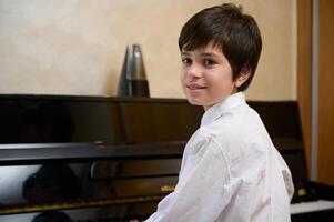 detailopname portret van een multi etnisch tiener jongen, weinig pianist musicus glimlachen op zoek Bij camera, zittend Bij piano forte foto