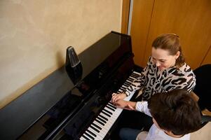 visie van bovenstaand van een Kaukasisch aangenaam volwassen vrouw muziek- docent, musicus pianist onderwijs piano, uitleggen naar een tiener leerling jongen de correct positie van vingers Aan de piano sleutels foto