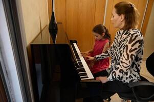 zelfverzekerd authentiek vrouw pianist, muziek- leraar geven een individu piano les naar haar weinig leerling. musical onderwijs en talent ontwikkeling in vooruitgang foto