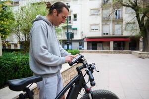 knap sportief Mens huren een elektrisch fiets gebruik makend van een verhuur app Aan mobiel telefoon. fiets sharing stad onderhoud. foto