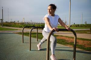 vol lengte portret van vrouw atleet oefenen met dwarsbalk Aan de stedelijk sportveld. foto