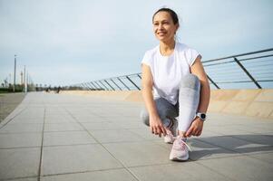 vrouw loper koppelverkoop veters Aan rennen schoenen, klaar voor joggen Aan de atlantic promenade Aan mooi zonnig zomer dag foto